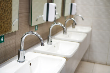 Side view of focused sinks with faucets arranged in the men's restroom of public restroom,  Thailand.