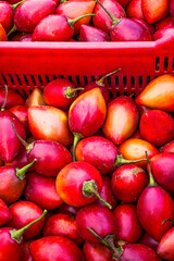 Fresh red tamarillos filling a red basket at the market