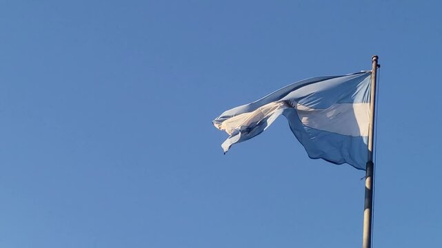 Argentine flag waving gently in the wind under a clear blue sky, symbolizing national pride and freedom, filmed 