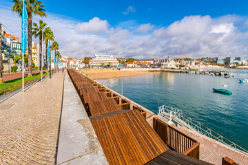 Obraz premium Avenue Dom Carlos, the waterfront tree lined street and promenade along the coast of the sandy beach and charming coastal town of Cascais, Portugal.