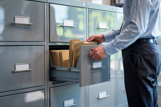 Business professional organizing files in a metal filing cabinet, maintaining records and documents