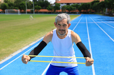 Senior Asian athlete using stretching rubber band warm up for running in the professional blue track for professional exercise, sport training workout and healthy for longevity