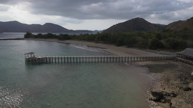 Aerial footage of harbor in Golo Mori Island beach with long bridge dock and sailing boats around.