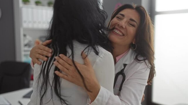 Woman doctor warmly hugging woman patient in clinic room, conveying empathy and care during medical consultation with a joyful atmosphere.