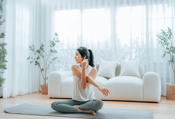Happy young Asian woman practicing yoga and shoulder stretching at home sitting on floor in living...