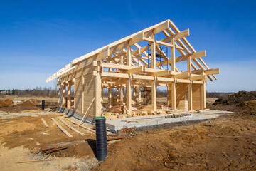 A wooden house frame under construction on a rural site with scattered materials and tools around....