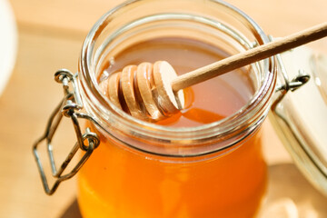 Golden honey fills a clear jar with a wooden dipper resting atop, illuminated by warm sunlight in a cozy setting perfect for culinary inspiration.