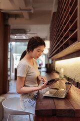Woman working on laptop and using calculator at cafe counter during casual financial planning session