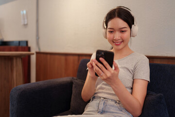 Young woman relaxing on sofa while listening to music with headphones and browsing songs on smartphone.
