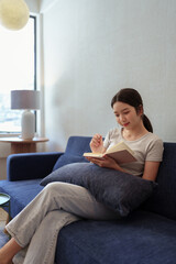 Calm young woman sitting on couch and writing in her diary during a peaceful moment in cozy home setting