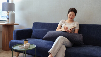Calm young woman sitting on couch and writing in her diary during a peaceful moment in cozy home setting