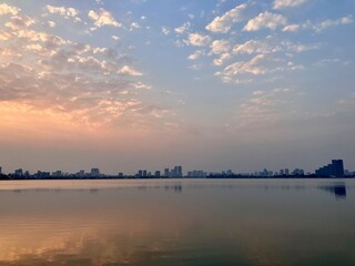Misty Dawn Serenity: Urban Skyline Meets Gentle Cloud Formations on West Lake in Hanoi, Vietnam