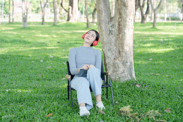 An Asian woman sits listening to music in a park. © Thitisak