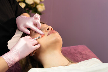 Clinician administers cheek filler injection on reclining patient. Aesthetic cosmetology. Lip Augmentation. Female client during procedure in beauty clinic