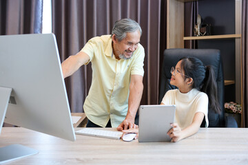 Young asian schoolgirl is doing her class homework assignment at home with advice from grandfather for education and study