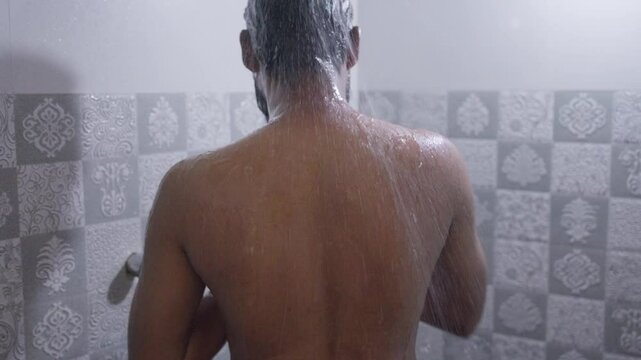 Back shot of a South Asian man taking a hot shower under bright natural light