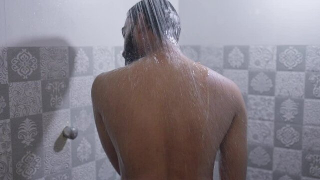 Back shot of a South Asian man rubbing his body with hot water in the shower