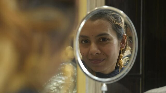 Young beautiful asian woman looking at mirror with 18k HUID certified gold earrings