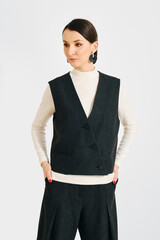Stylish woman poses in a tailored dark vest and light sweater against a neutral backdrop