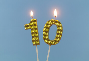 Burning golden birthday candles on blue background, number 10