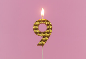 Burning gold birthday candle on pink background, number 9