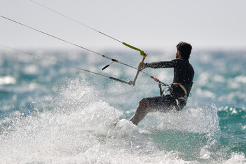A dynamic photo capturing a kitesurfer in action, riding a wave while performing a maneuver. 