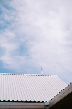 Rippled metal roof with lightning rod against blue sky and fluffy clouds