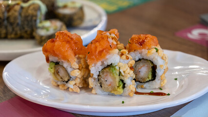 Close-up of colorful sushi rolls with crispy rice coating, avocado, shrimp tempura, and spicy salmon topping served on a ceramic plate in a Japanese restaurant