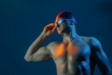 Focused swimmer in goggles and cap, lit by contrasting lights, ready to dive into action.