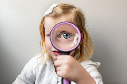 Girl holding magnifying glass in front of one eye indoors.