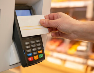 Buyer hand makes payment with bank card at POS terminal for purchases in supermarket close-up