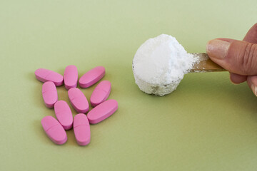 A spoonful of creatine in a woman's hand and pink vitamin capsules. Sports supplements for active women.