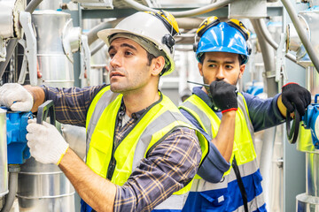 Two technicians man in hard hats and safety vests carefully inspect and repair complex machinery in...