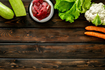 Natural pet food in feeding bowl and ingredients meat and vegetables, top view