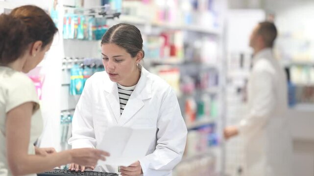 Young female pharmacist giving prescription medicine to adult female buyer at pharmacy