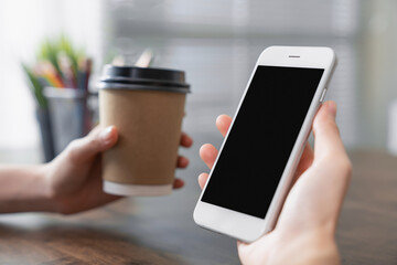 Hand holding smartphone with a blank screen on table, for putting advertising to promote.