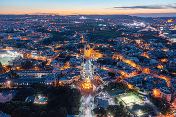 Fototapeta premium Panoramic view of Lija village in Malta. The Belveder Tower and Parish Church are lit. Mdina can be see in the distance during just after sunset.