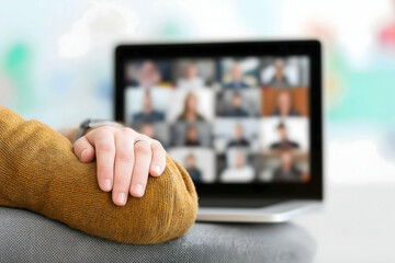 A person rests their hand on a couch while participating in a virtual meeting displayed on a laptop screen.