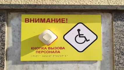Inscription in Russian: Attention Staff call button. Accessible environment for people with disabilities. Yellow information sign with Braille. Close-up help button for people with limited mobility