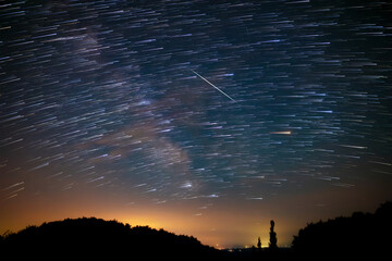 Star trails of a Milky Way with meteor, shooting stars and countryside silhouettes.