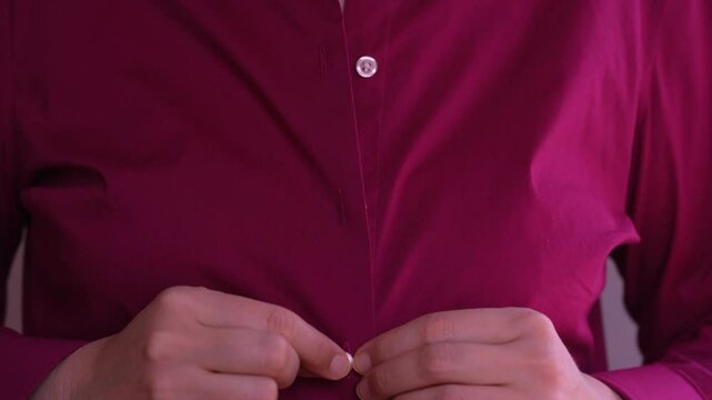 Woman unbuttoning the buttons of her burgundy shirt.
