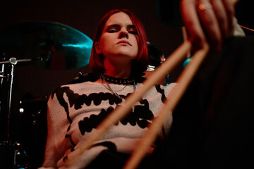 Portrait of confident female drummer wearing spiked choker necklace, captured sitting with...