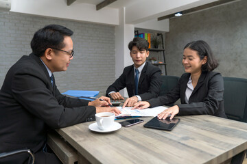 Three professional engage in a focused discussion around a conference table, reviewing document and presenting ideas in a contemporary office environment.