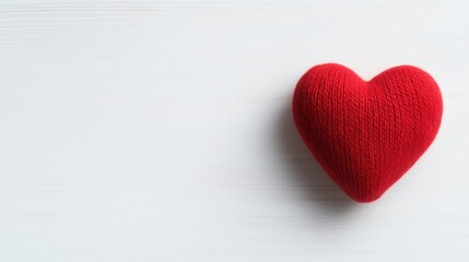 Fototapeta premium A red knitted yarn heart is placed on a white wooden background with copy space on the left side.