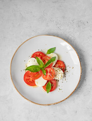 Caprese salad with sliced ​​tomatoes, mozzarella and basil on a plate on a light background