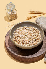 Oat flakes in bowl with wheat on a wooden board on a yellow background.