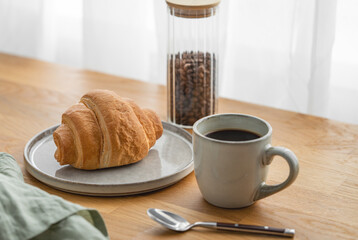 Cup of freshly brewed coffee on a wooden table with croissants