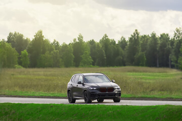 Fototapeta premium Expensive black SUV on a scenic road with lush green fields