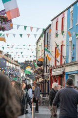 Festive street scene in Galway, Ireland, with colorful facades, Irish flags, and people walking...