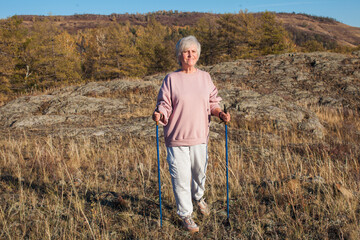 Attractive short haired middle aged woman in activewear hiking in forest using poles for nordic walking